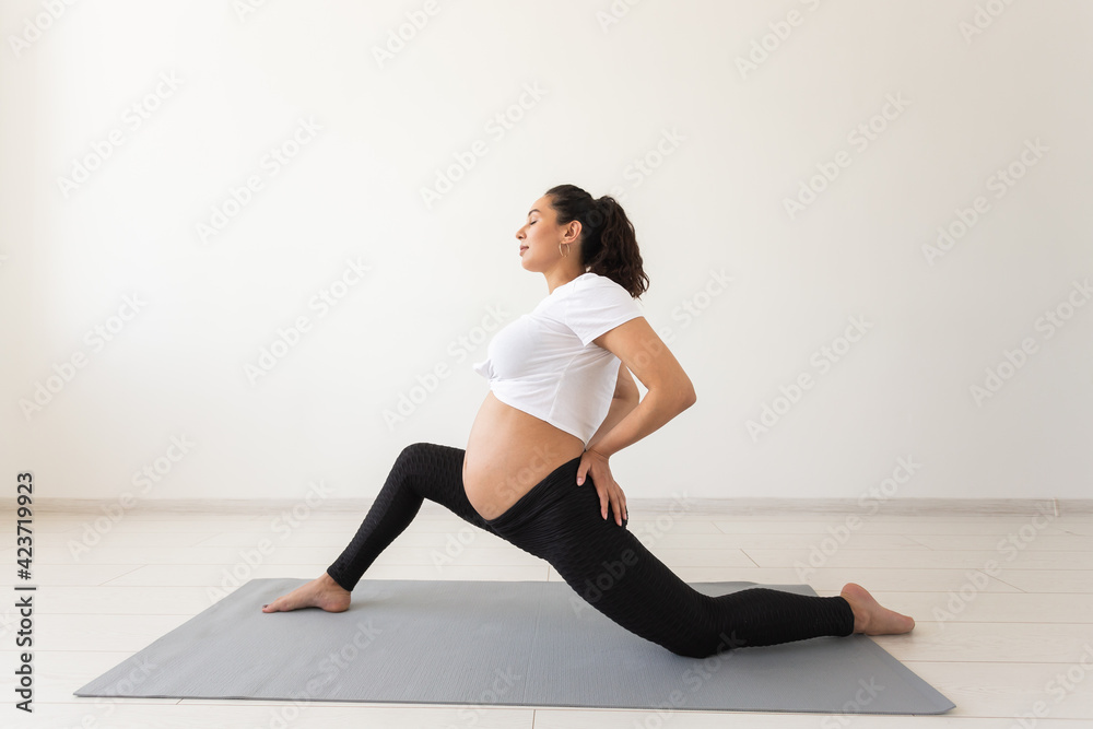 Young flexible pregnant woman doing gymnastics on rug on the floor on white background. The concept of preparing the body for easy childbirth Young flexible pregnant woman doing gymnastics on rug on the floor on white background. The concept of preparing the body for easy childbirth