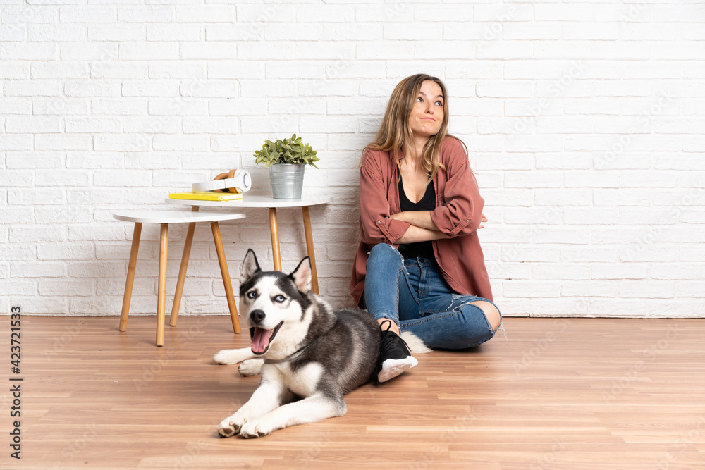 Young girl with her dog sitting in the floor at indoors making doubts gesture while lifting the shoulders Young girl with her dog sitting in the floor at indoors making doubts gesture while lifting the shoulders
