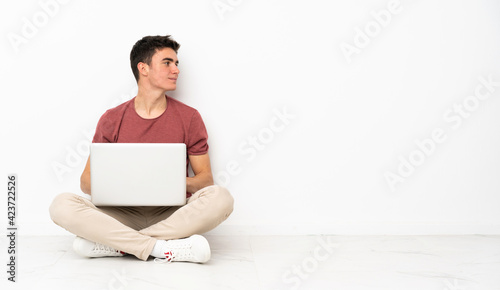 Teenager man sitting on the flor with his laptop in lateral position