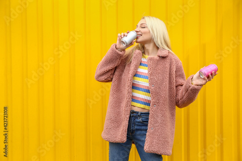 Beautiful young woman drinking soda on color background