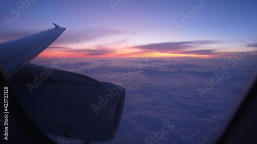 Look out from airliner window to sunset afterglow at horizon and blue clouds covering all area down. Scenic view of sky from passenger plane flying on cruise altitude at late evening hour