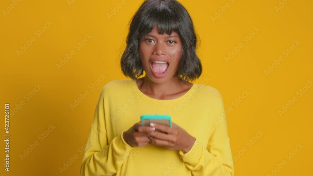 Shocked dark skinned young woman feels surprised looks with disbelief at camera points at smartphone display fascinated by exciting news or received comments on her blog post. Omg look there Shocked dark skinned young woman feels surprised looks with disbelief at camera points at smartphone display fascinated by exciting news or received comments on her blog post. Omg look there