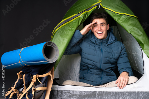 Teenager caucasian man inside a camping green tent isolated on black background has just realized something and has intending the solution