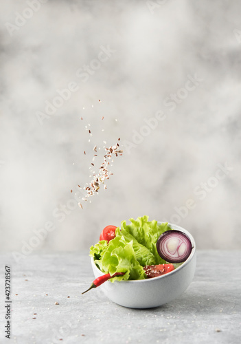 bowl with fresh lettuce and seeds in levitation on gray stone background