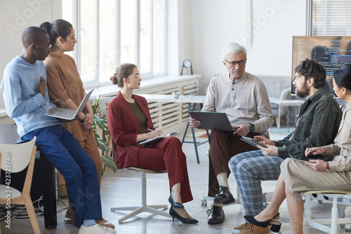 Wide angle view at contemporary diverse business team sitting in circle during strategy meeting, focus on senior businessman in center