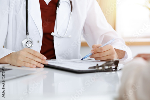 Unknown woman-doctor filling up an application form while consulting patient. in sunny room Medicine concept