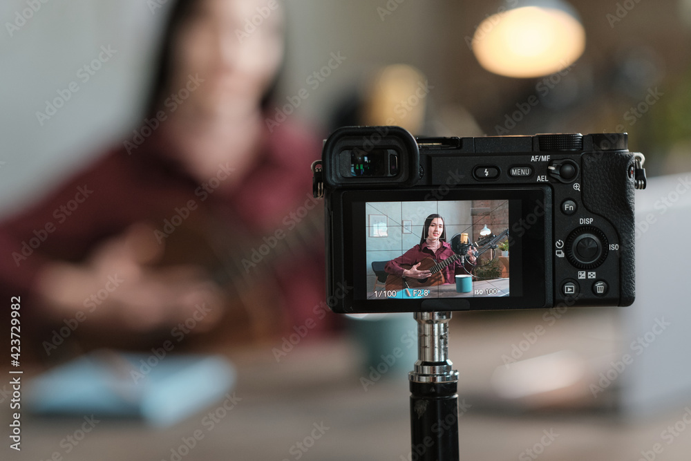Young woman playing guitar and recording her performance on the camera in the room Young woman playing guitar and recording her performance on the camera in the room
