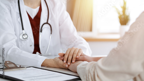 Hands of unknown woman-doctor reassuring her female patient in sunny room, close-up