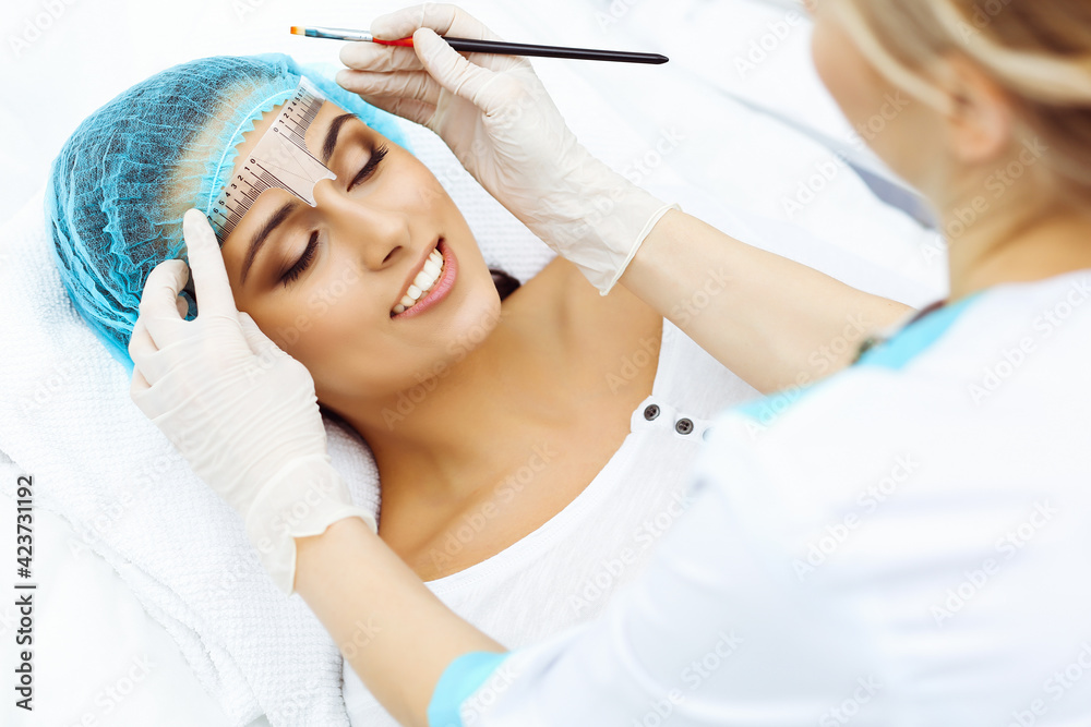 © rogerphoto - Professional beautician is going to correct eyebrow line at woman face using cosmetic ruler. Permanent brow makeup in beauty salon, closeup. Cosmetology treatment © rogerphoto - Professional beautician is going to correct eyebrow line at woman face using cosmetic ruler. Permanent brow makeup in beauty salon, closeup. Cosmetology treatment