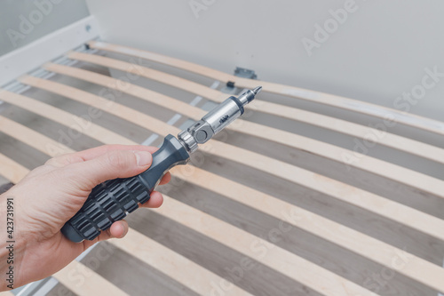 Assembling a frame for a mattress with wooden planks called a rack-and-pinion bed base using a screwdriver. photo