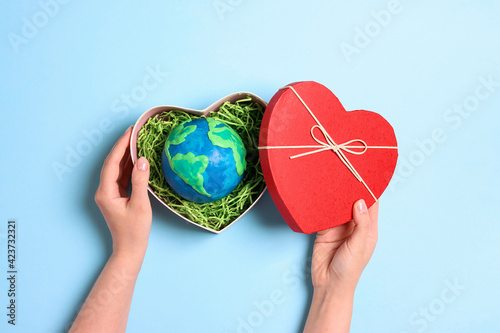 Fototapeta Naklejka Na Ścianę i Meble -  Female hands holding heart gift box with planet earth on a blue background. Earth Day.