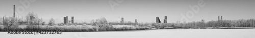 An abandoned old chemical plant on the bank of a frozen winter river covered with snow