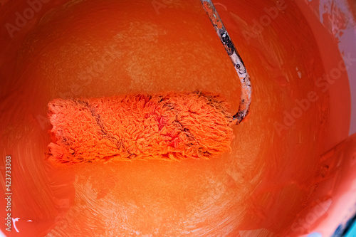 Paddle roller with orange wet paint in bucket