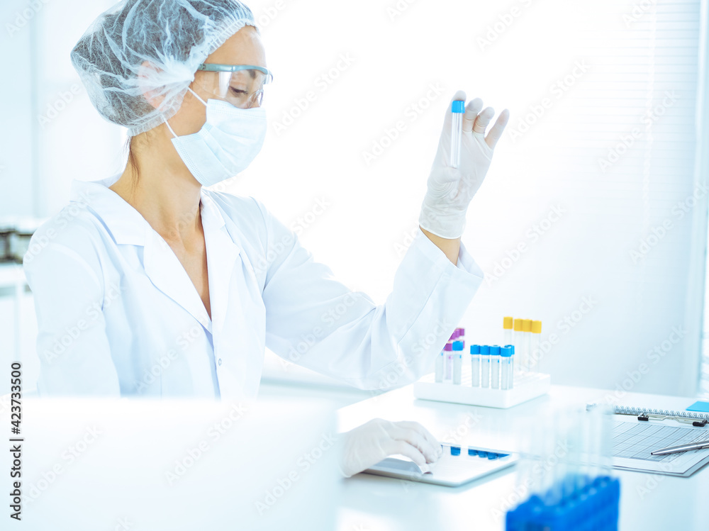Professional female scientist in protective eyeglasses researching tube with reagents in laboratory toned in blue. Concepts of medicine and science researching