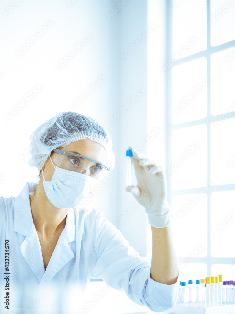 Professional female scientist in protective eyeglasses researching tube with reagents in laboratory toned in blue. Concepts of medicine and science researching