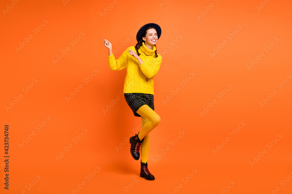 Full size photo of optimistic cute girl dance wear yellow sweater cap skirt shoes isolated on orange background