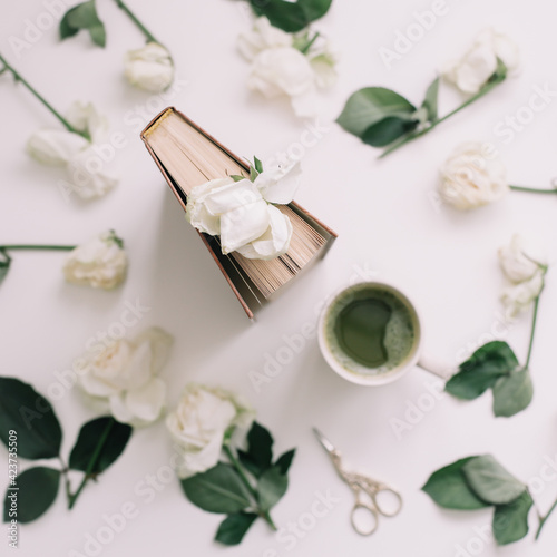 A book with white roses and a cup of green tea on a white background, top view