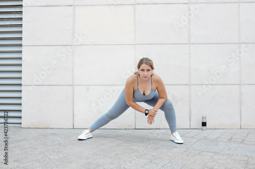 Fototapeta Naklejka Na Ścianę i Meble -  Tired unhappy plus size young woman doing side lunges and leaning forward to open up tight hips and groin, while strengthening inner thigh and glutes