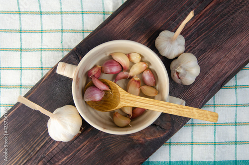 Unpeeled garlic in a bowl on a wooden cutting board.