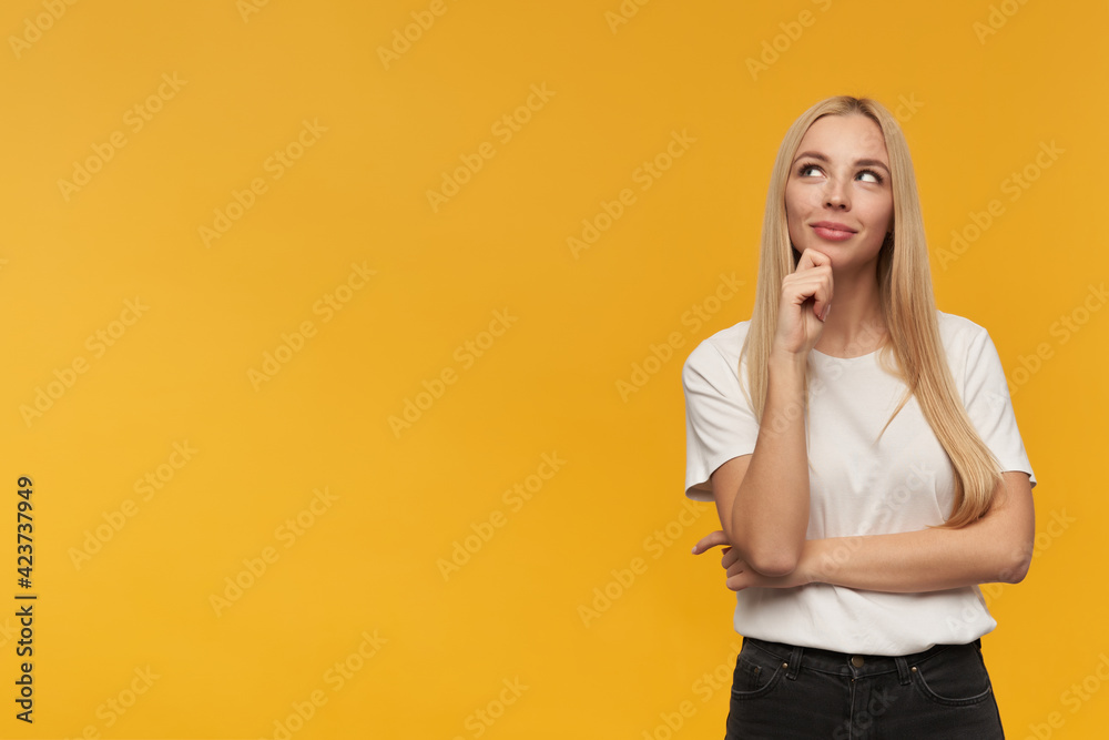 Teenage girl, happy looking woman with blond long hair. Wearing white t-shirt and black jeans. People and emotion concept. Watching to the left at copy space, isolated over orange background Teenage girl, happy looking woman with blond long hair. Wearing white t-shirt and black jeans. People and emotion concept. Watching to the left at copy space, isolated over orange background