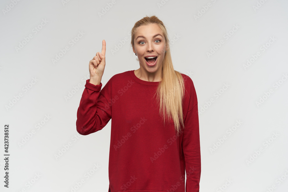 Portrait of attractive, adult girl with blond long hair. Wearing red sweater. People and emotion concept. Watching at the camera, keeps her finger up isolated over white background Portrait of attractive, adult girl with blond long hair. Wearing red sweater. People and emotion concept. Watching at the camera, keeps her finger up isolated over white background