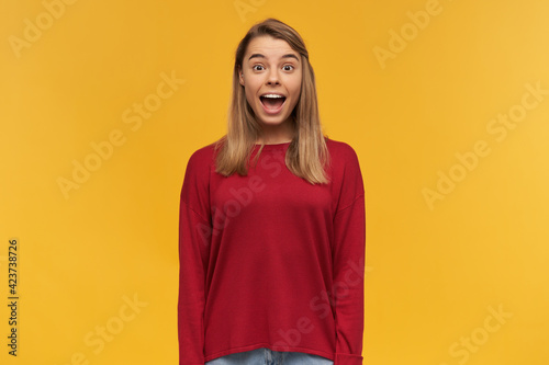Close up of surprised blonde young girl, standing with mouth wide opened in amazement. OMG concept. Isolated on a yellow studio background © timtimphoto