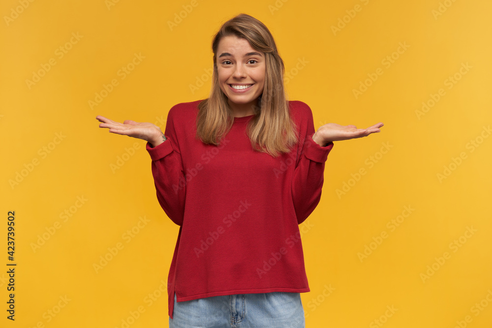 Confused young girl shrugging shoulders, having guilty look, feeling sorry for doing something wrong and making terrible mistake, dressed in red sweater, isolated on a yellow studio background Confused young girl shrugging shoulders, having guilty look, feeling sorry for doing something wrong and making terrible mistake, dressed in red sweater, isolated on a yellow studio background