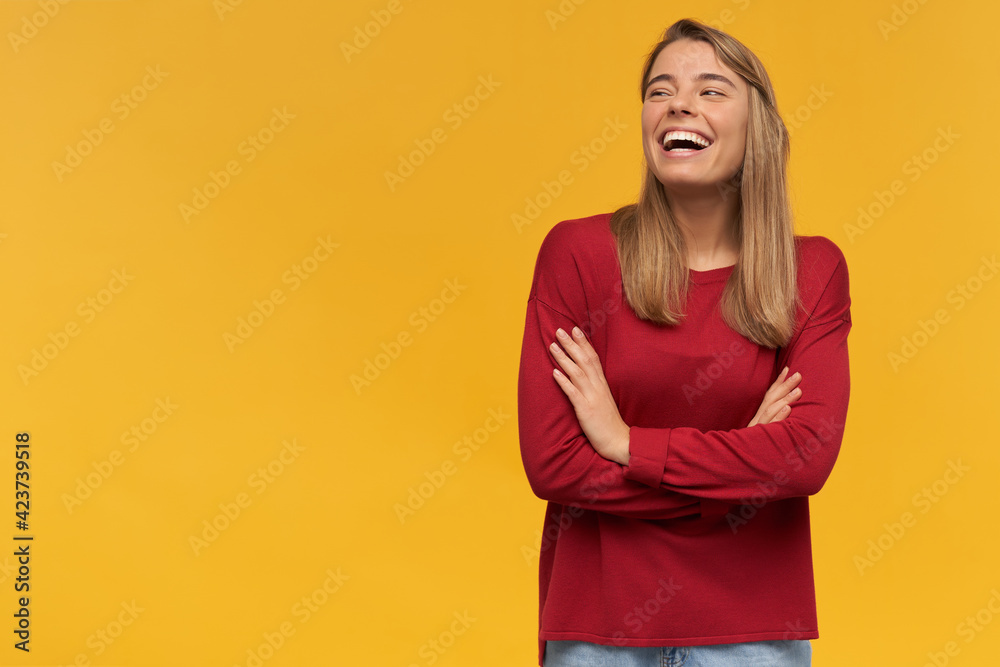 Laughing happy girl, turned to the left side, stands with folded arms isolated on a yellow background. Funny joke, pleasant moment, free space for your advertisement Laughing happy girl, turned to the left side, stands with folded arms isolated on a yellow background. Funny joke, pleasant moment, free space for your advertisement