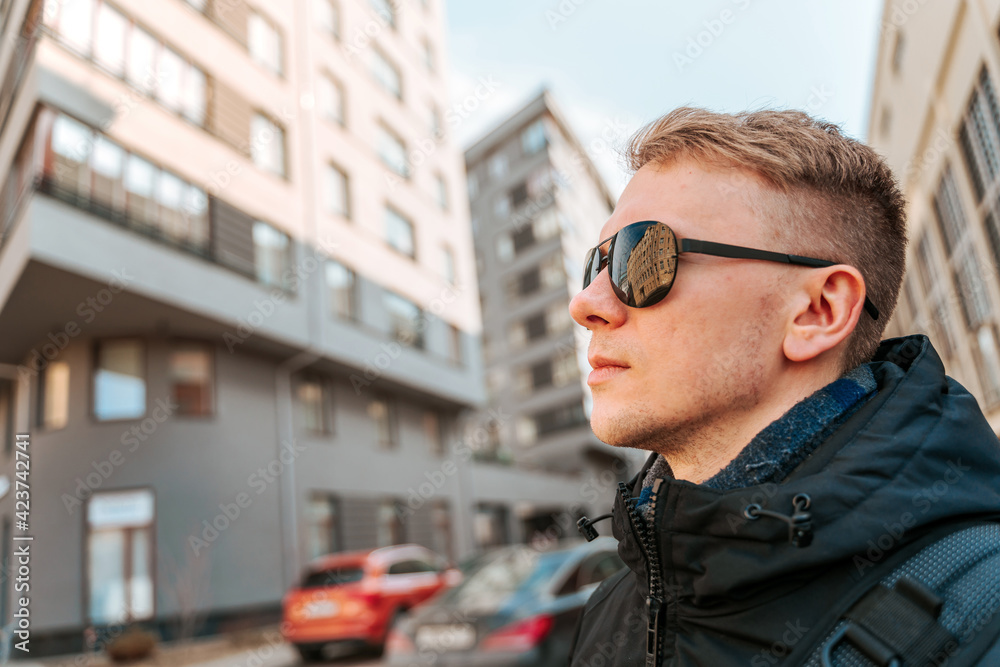 A young man in a jacket and sunglasses stands in the financial district near the business buildings A young man in a jacket and sunglasses stands in the financial district near the business buildings