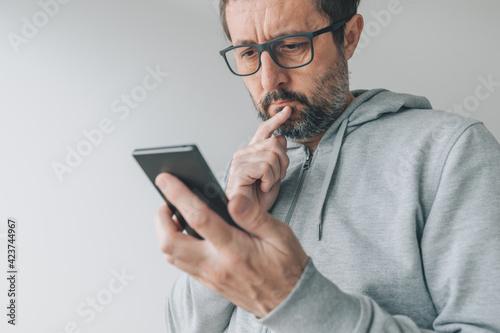 Obraz na plátně Serious thoughtful mid-adult male looking at mobile smart phone screen with fing