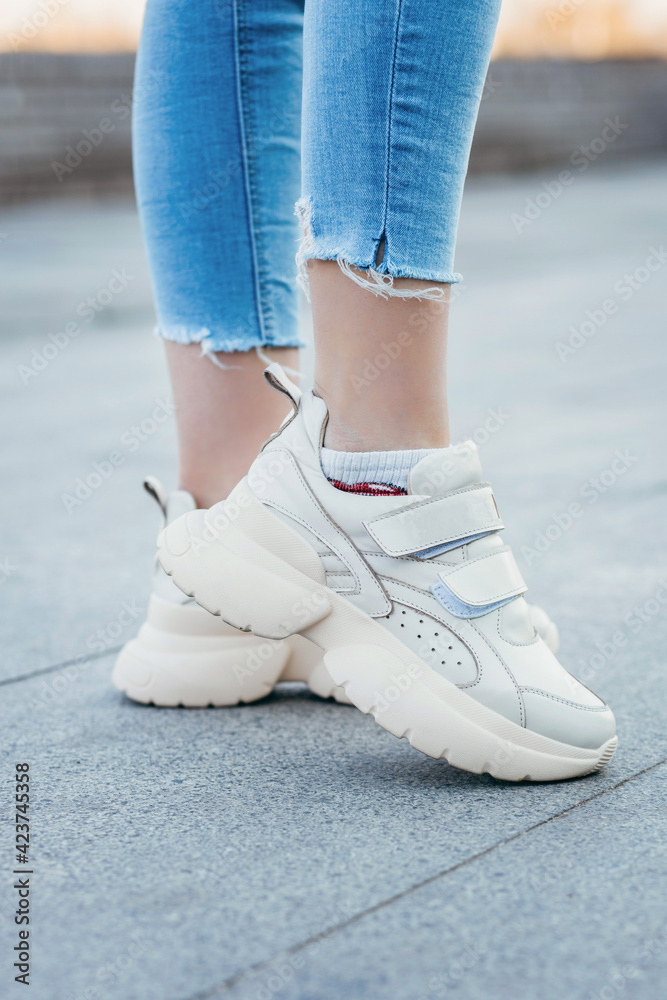 White sneakers on girl legs on the street background