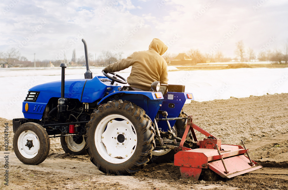 Obraz premium Farmer on a tractor with milling machine loosens, grinds and mixes soil. Loosening the surface, cultivating the land for further planting. Farming and agriculture. Cultivates the soil. Plows a field.