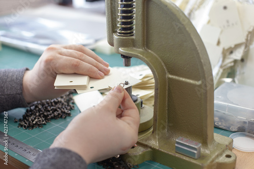 фотографія close-up hands man put grommets and eyelet in a stack of blanks clothing tags on a large manual press professional grommet machine