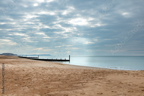 A scenics view of a sandy beach at low tides with wooden groynes  breakwaters   sandy beach along a calm sea under a majestic marble sky with some ray of light