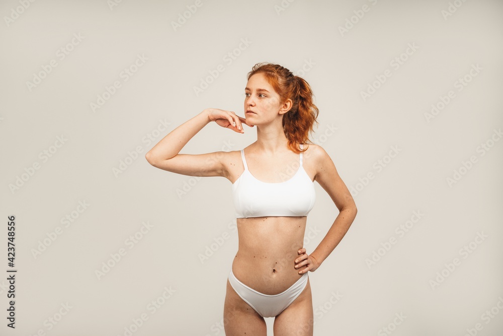 Obraz premium Portrait of cute redhead young woman with long wavy hair and freckles wears white underwear. Isolated over white background. Natural beauty and health