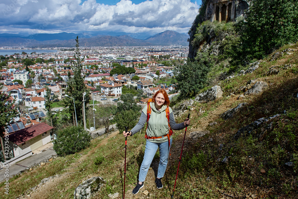 Young woman walks near rock-cut tombs of ancient Lycia in Fethiye, Turkey.