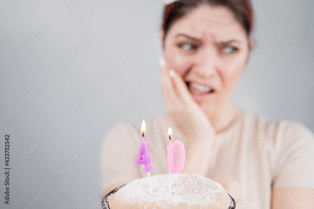 Unhappy woman holding a cake with candles for her 40th birthday. The girl cries about the loss of youth. Unhappy woman holding a cake with candles for her 40th birthday. The girl cries about the loss of youth.