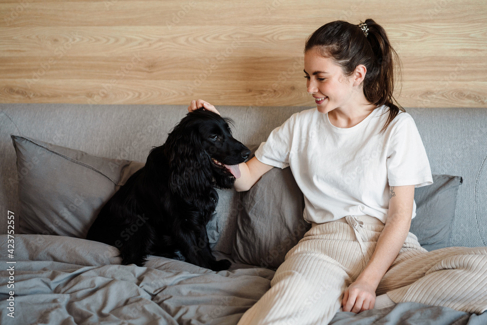 Obraz premium Smiling young brunette woman petting her dog at home
