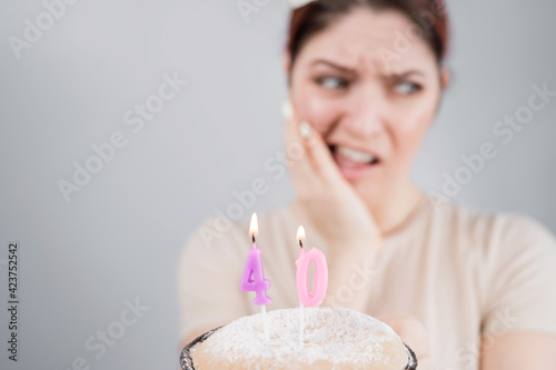 Unhappy woman holding a cake with candles for her 40th birthday. The girl cries about the loss of youth.