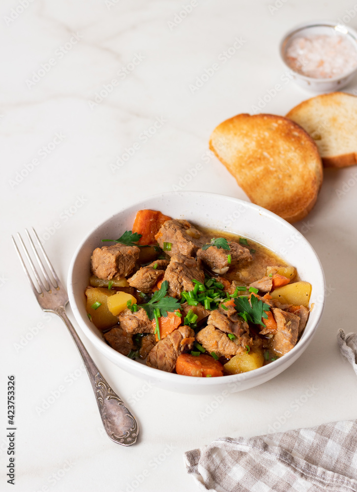 Goulash, beef stew with vegetables and thyme in a white plate with onion and greens.