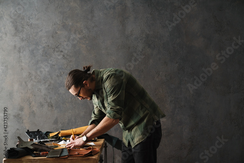 Bearded focused craftsman working with leather while standing at table