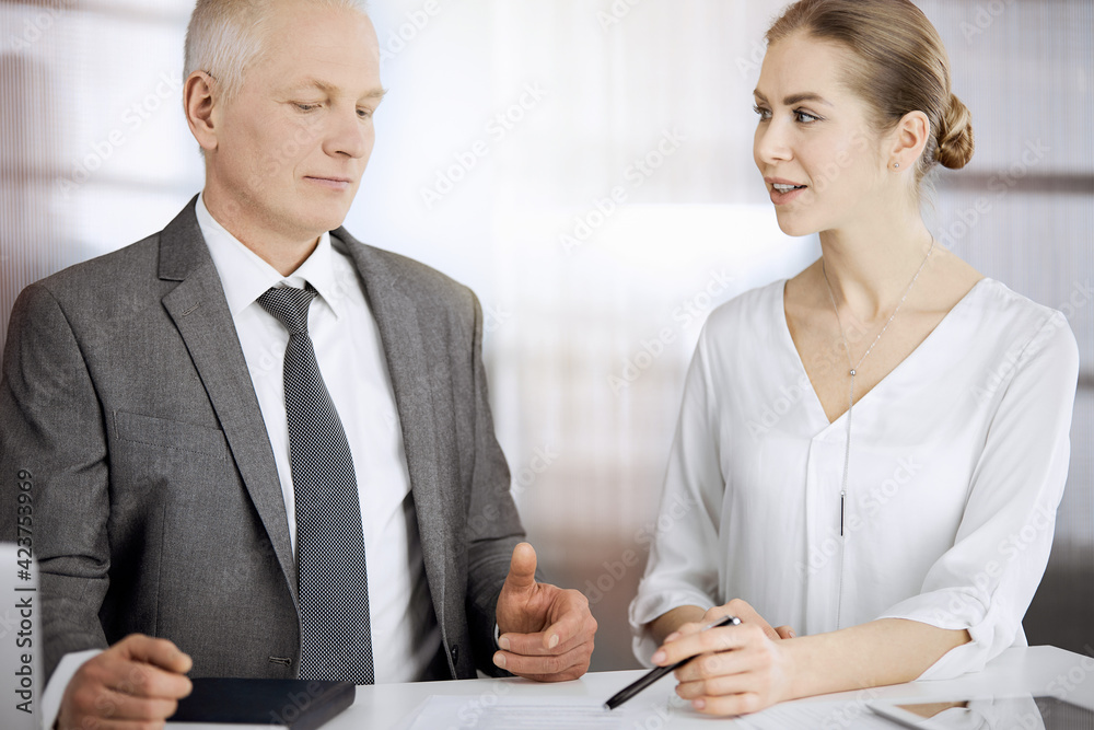Elderly businessman and woman sitting and communicating in sunny office. Adult business people or lawyers working together as a partners and colleagues at meeting Elderly businessman and woman sitting and communicating in sunny office. Adult business people or lawyers working together as a partners and colleagues at meeting