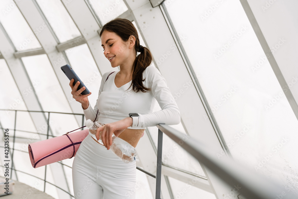 Brunette smiling sportswoman using mobile phone while leaning on railing Brunette smiling sportswoman using mobile phone while leaning on railing
