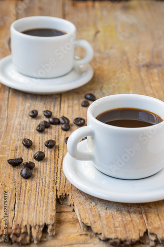 Top view of two white cups of coffee, on rustic wooden table with coffee beans, selective focus, vertical