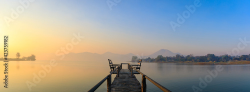 Panorama or panoramic landscape photo of Lake and mountain on the background with a little white fog sunshine light on the morning. and wooden bridge with seat for sit.