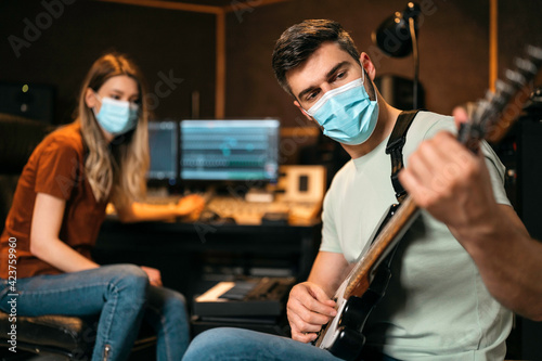 Teamwork by band musicians wearing masks working in studio and playing guitar
