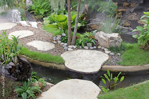 A small stepping stone syle bridge over a manmade stream in manicured tropical garden with rocks  grass and flowers  southeast Asia
