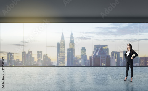 Businesswoman standing in an empty loft room with a panoramic window, city view, concrete floor, real estate, advertising concept