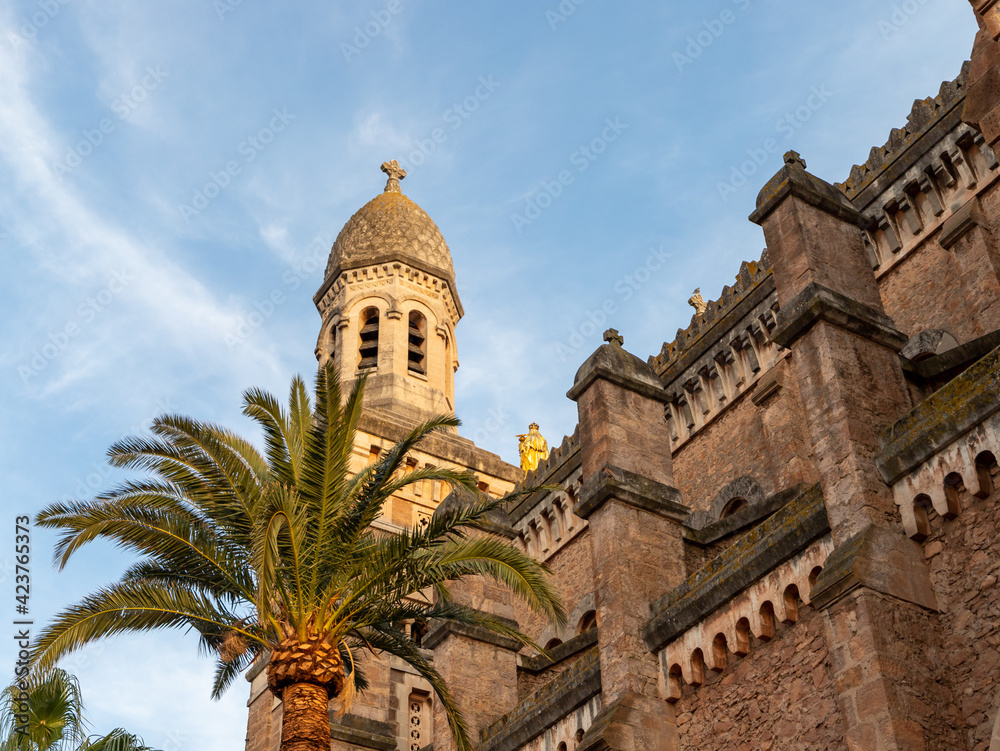 an old church tower in the evening glow. a palm tree stands in front of an old building. Vacation in France. 