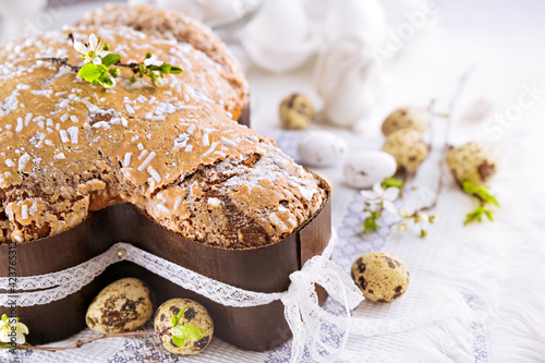 Traditional Italian desserts for Easter - Easter dove. Festive pastries with almonds and sugar icing on a light background and flowering branches  Easter decor and eggs. close-up